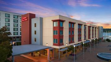 Un hotel con diseño moderno, que destaca por su fachada roja y blanca, un área exterior cubierta y vistas a la marina al fondo.
