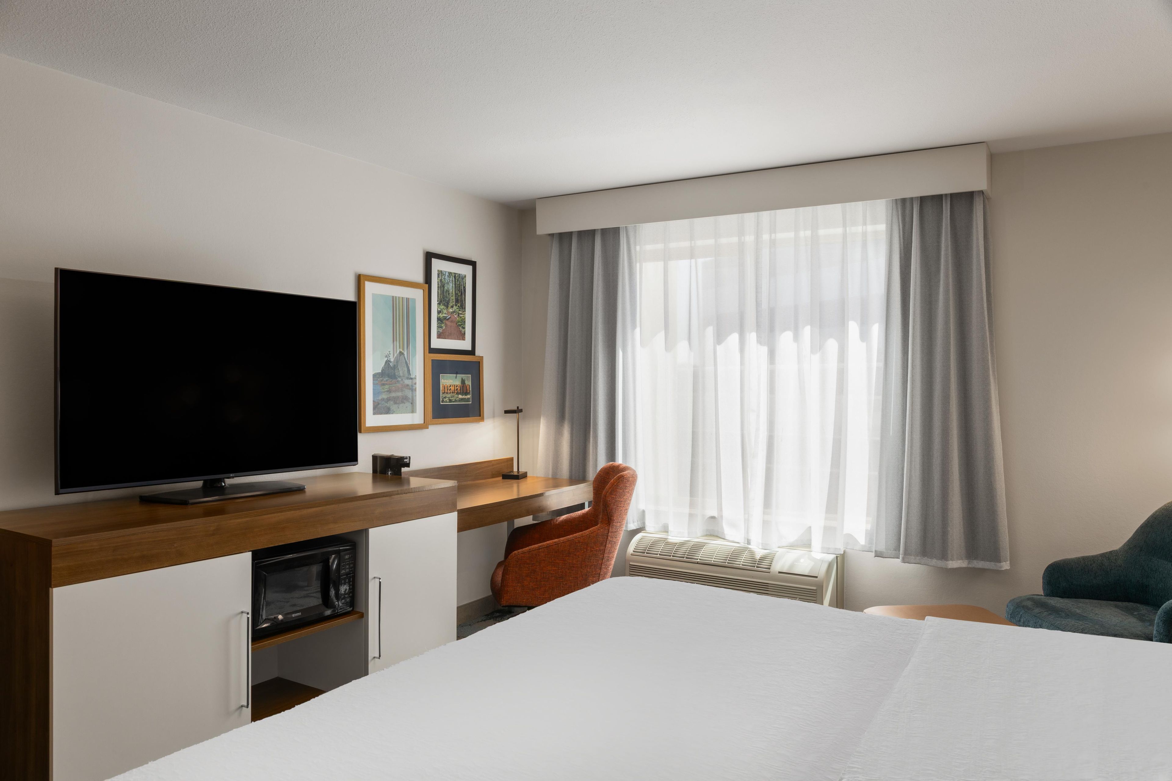 Een hotelkamer met een groot bed, een flatscreen televisie, een bureau met stoel en een raam met gordijnen.