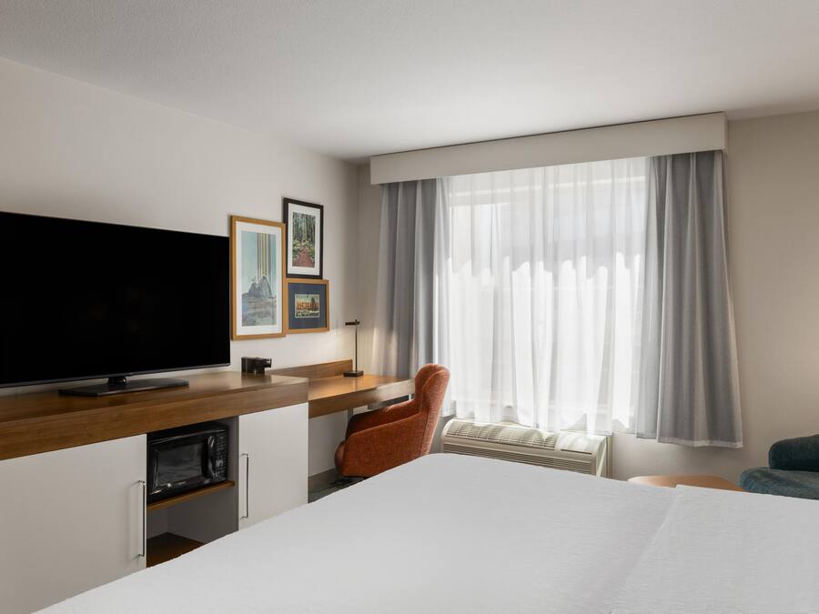A hotel room with a large bed, a flat-screen TV, a desk with a chair, and a window with curtains.