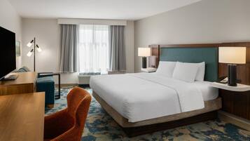 A hotel room with a large bed, two bedside tables with lamps, a desk, a chair, and a television.