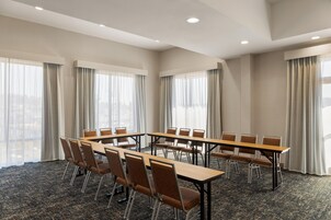 Un salón de conferencias con una larga mesa y sillas, ventanas grandes con cortinas y suelo alfombrado.