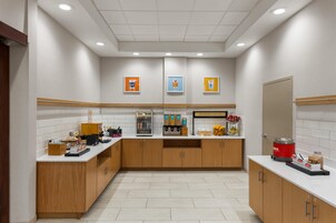 A modern breakfast area with a self-serve station, a refrigerated display case, and a sign that reads 'HAPPY BREAKFAST STARTS HERE'.