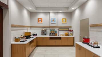 A modern breakfast area with a self-serve station, a refrigerated display case, and a sign that reads 'HAPPY BREAKFAST STARTS HERE'.
