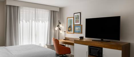 A hotel room with two beds, a desk with a flat-screen TV, a chair, and artwork on the wall.