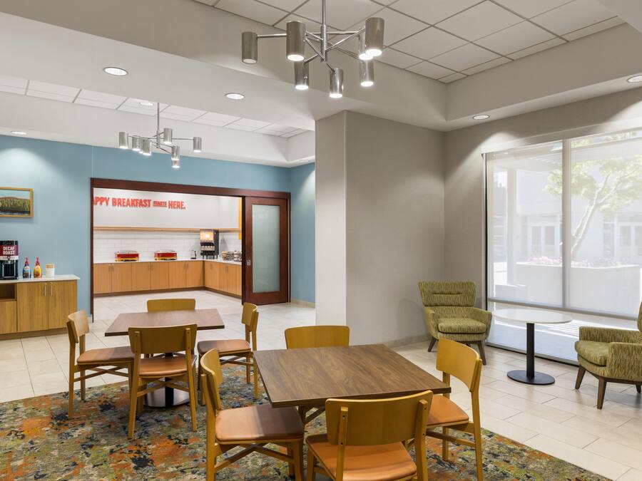 A modern dining area with a breakfast bar, wooden chairs, a patterned rug, and a large window offering a view.