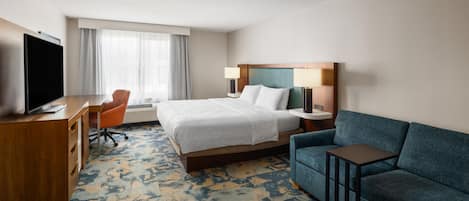 Quarto de hotel com cama, escrivaninha com televisão, sofá e janela com cortinas.