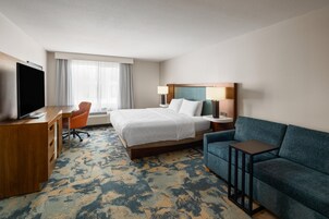 Quarto de hotel com cama, escrivaninha com televisão, sofá e janela com cortinas.