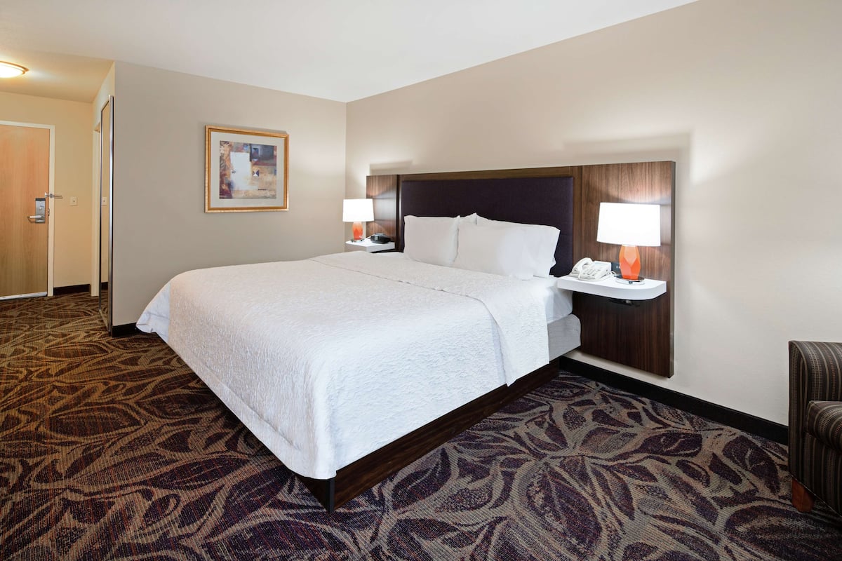 A hotel room with a large bed, two bedside tables with lamps, a framed picture on the wall, and a patterned carpet.