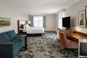 Quarto de hotel com cama, escrivaninha, televisão, cadeira e sofá.