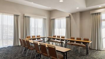 A conference room with a long table and chairs, large windows with curtains, and a carpeted floor.