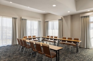 A conference room with a long table and chairs, large windows with curtains, and a carpeted floor.