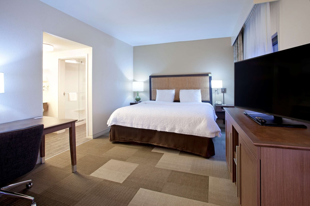 Une chambre d’hôtel avec un grand lit, un bureau, une télévision et une salle de bain visible à travers une porte ouverte.