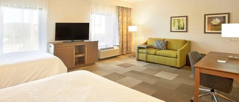 A hotel room with two beds, a television, a desk, a chair, a sofa, and a lamp.
