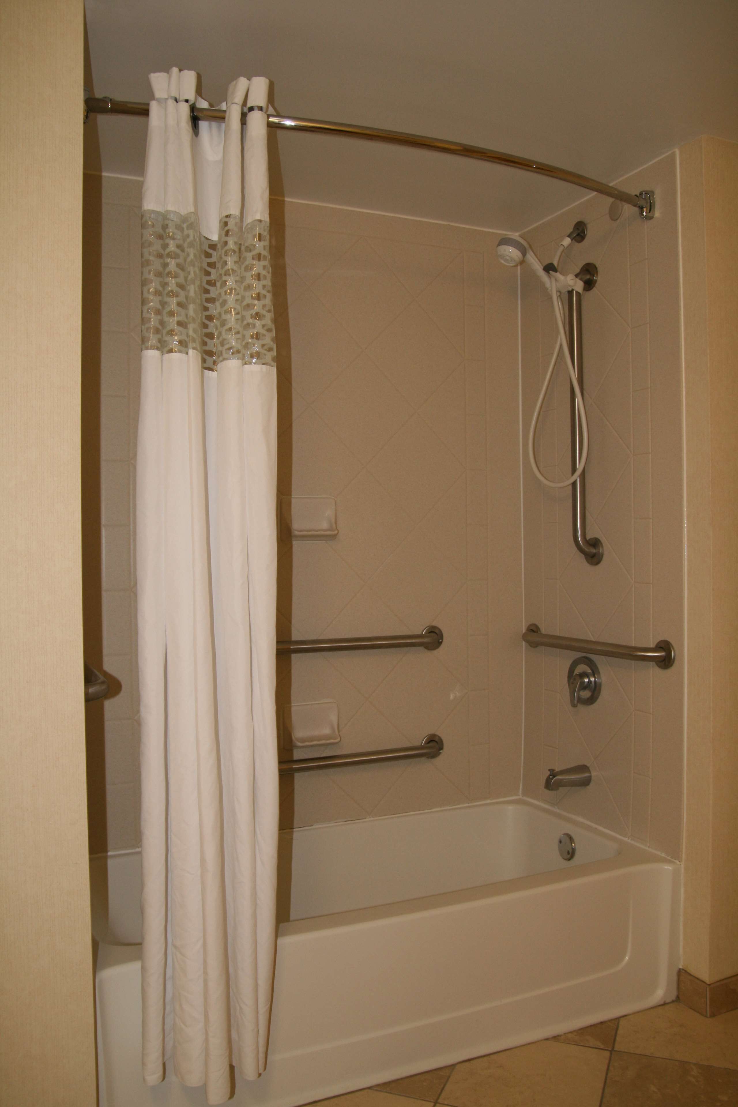 A walk-in shower with a glass door, grab bars, and a handheld showerhead.