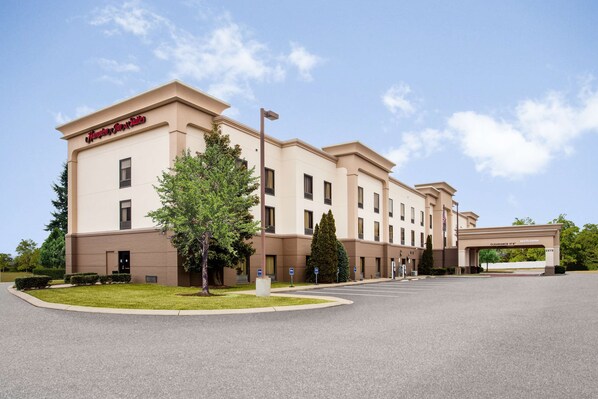 Ein Hampton Inn Hotel mit einer übersichtlichen Auffahrt, einem einladenden Bogen und einem gepflegten Rasen.