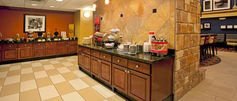 Cocina de hotel con suelo a cuadros, armarios de madera y una pared de acento de piedra.