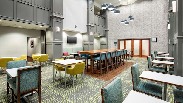 Un hall d’hôtel comprenant un bar, des espaces aménagés avec des sièges et un écran de télévision.