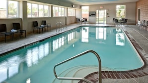 Une piscine intérieure à l’eau claire, entourée de chaises et de tables, et dotée de grandes fenêtres qui laissent entrer la lumière naturelle.
