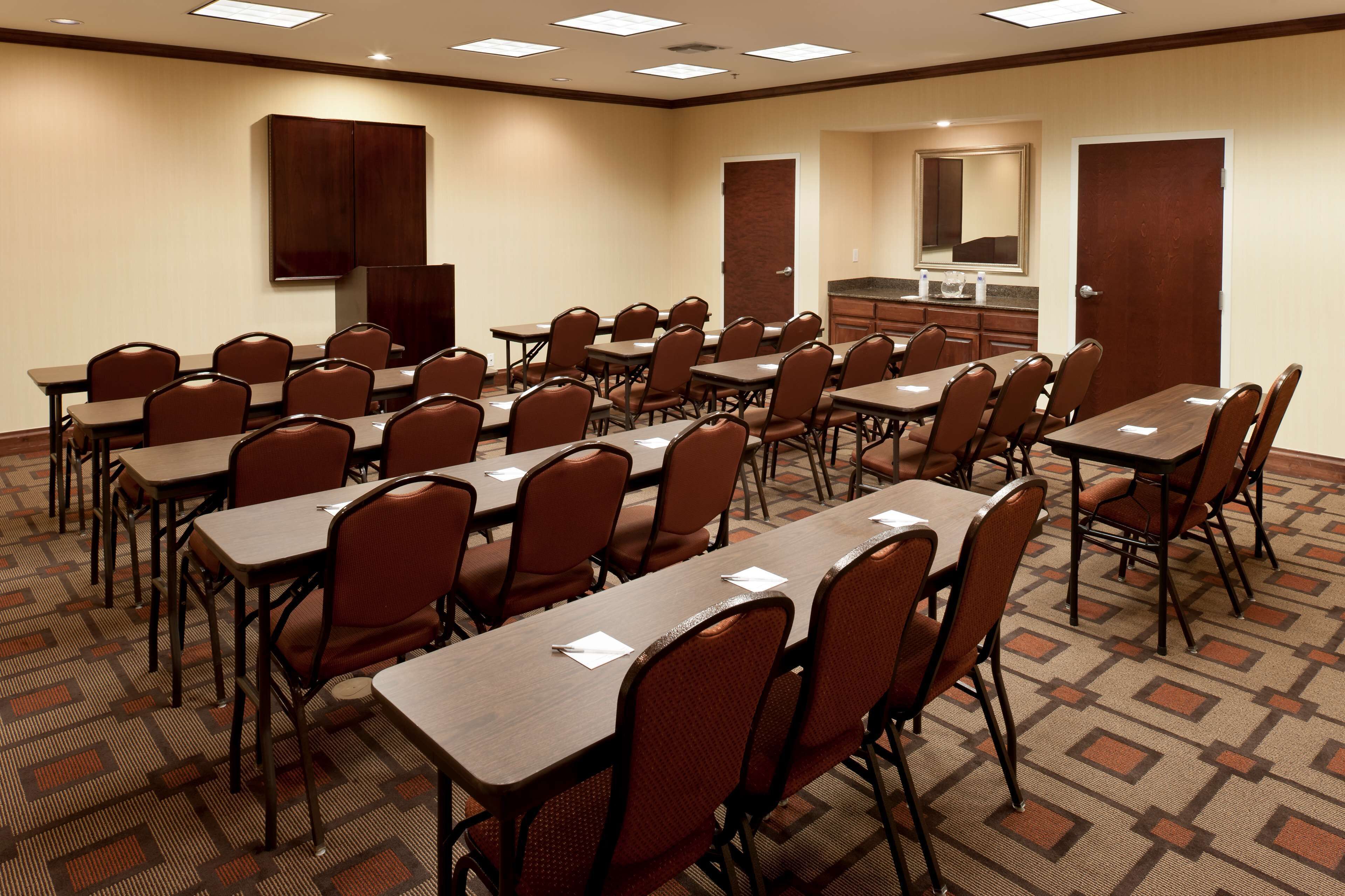 Une salle de conférence équipée de plusieurs tables et chaises, d’un coin cuisine et d’une porte.