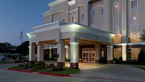 Un bâtiment de l’hôtel Hampton Inn & Suites, avec une entrée bien visible, un mât de drapeau et une façade bien éclairée.