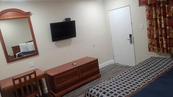 Un dormitorio con cama, cómoda, escritorio, silla, espejo, televisor y puerta.