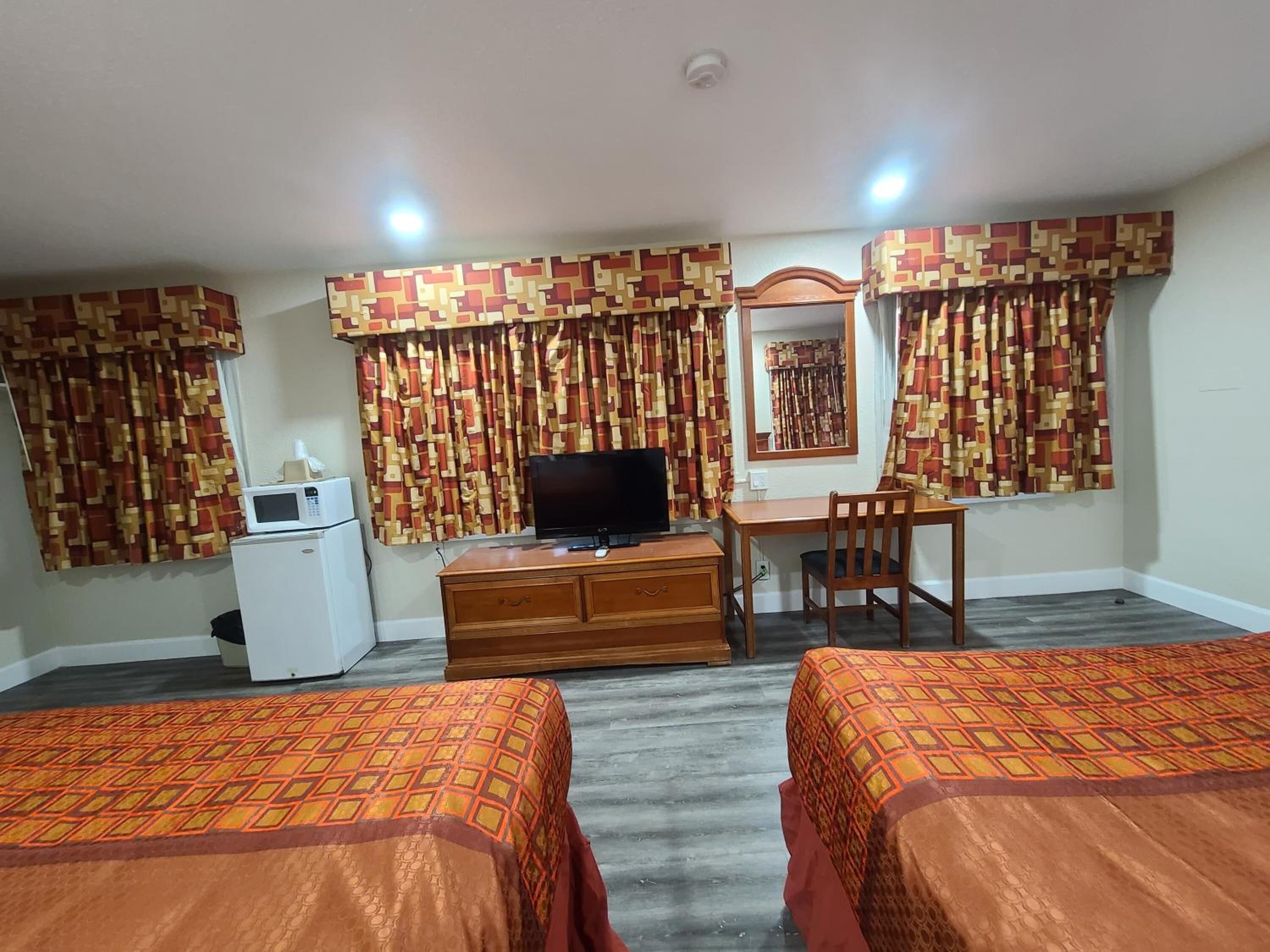 A hotel room with two beds, a desk, a television, a microwave, and patterned curtains.