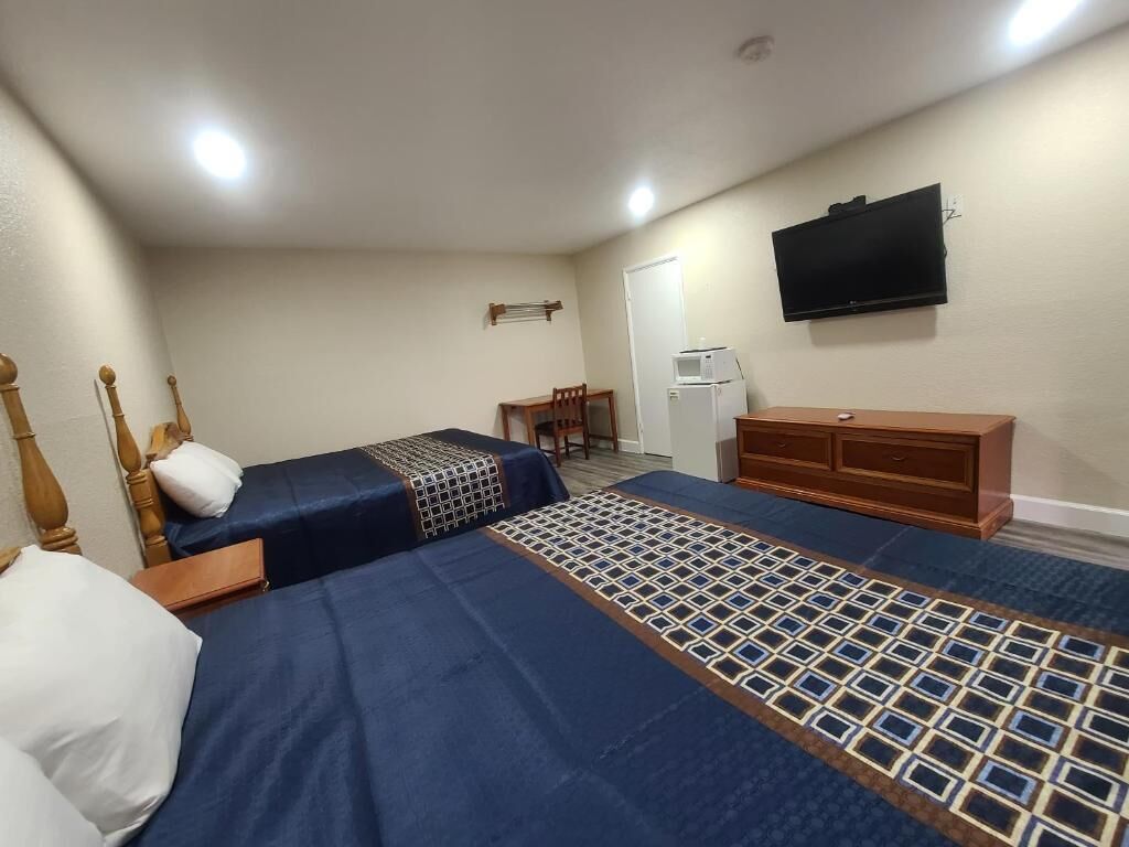 Habitación de hotel con dos camas, un televisor montado en la pared, un escritorio pequeño y un refrigerador.