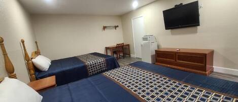 Habitación de hotel con dos camas, un televisor montado en la pared, un escritorio pequeño y un refrigerador.
