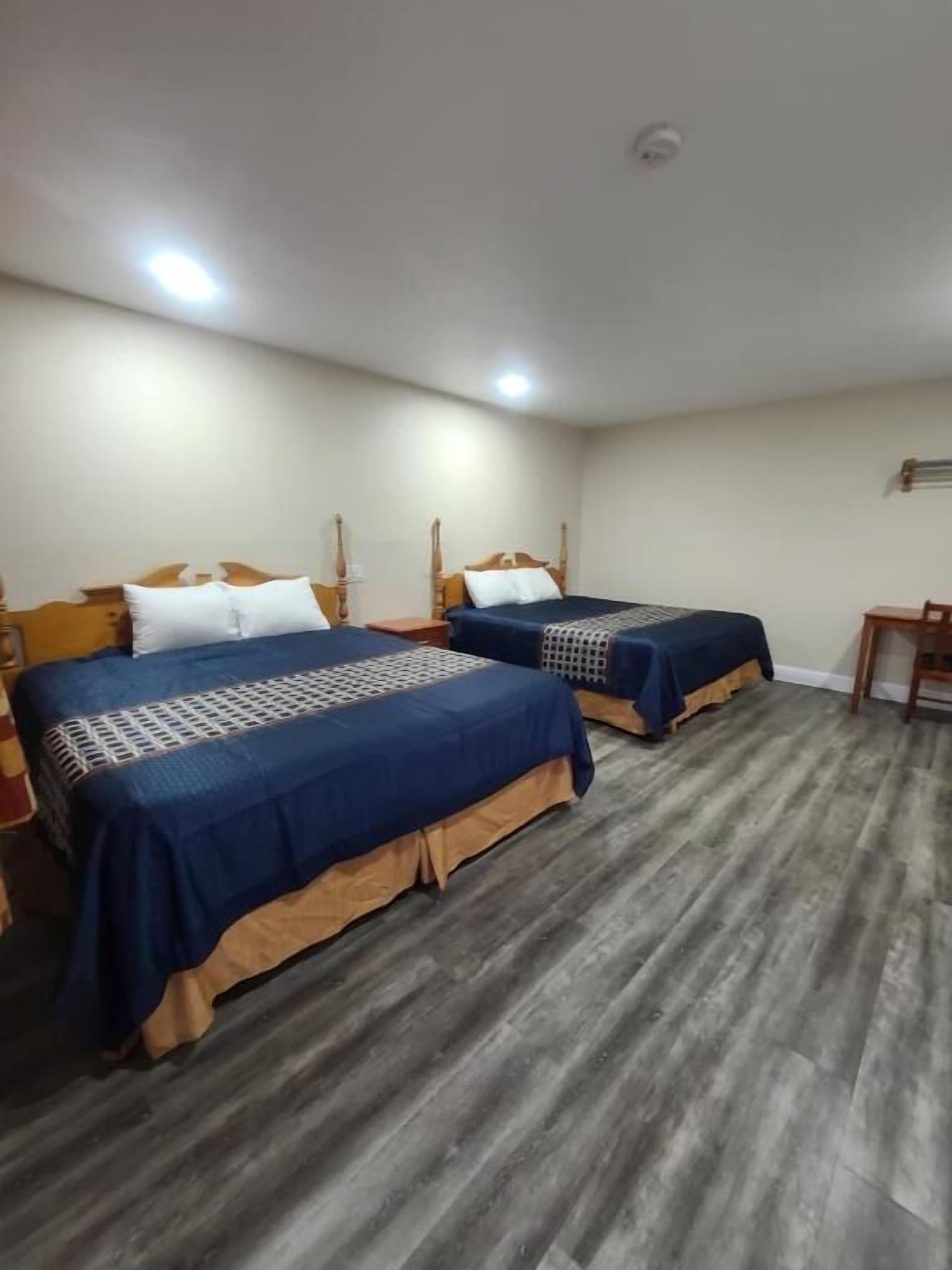 A hotel room with two beds, wooden headboards, and a small table.