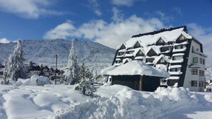Un bâtiment recouvert de neige, avec un toit en pente, entouré de congères et d’arbres.