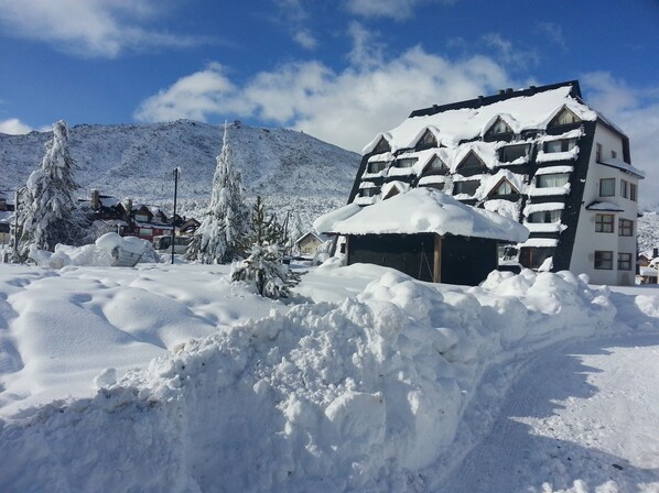 A snow-covered building with a sloped roof, surrounded by snowbanks and trees.