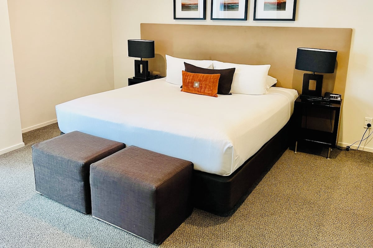 A hotel room with a large bed, two bedside tables with lamps, a headboard, and three framed pictures on the wall.