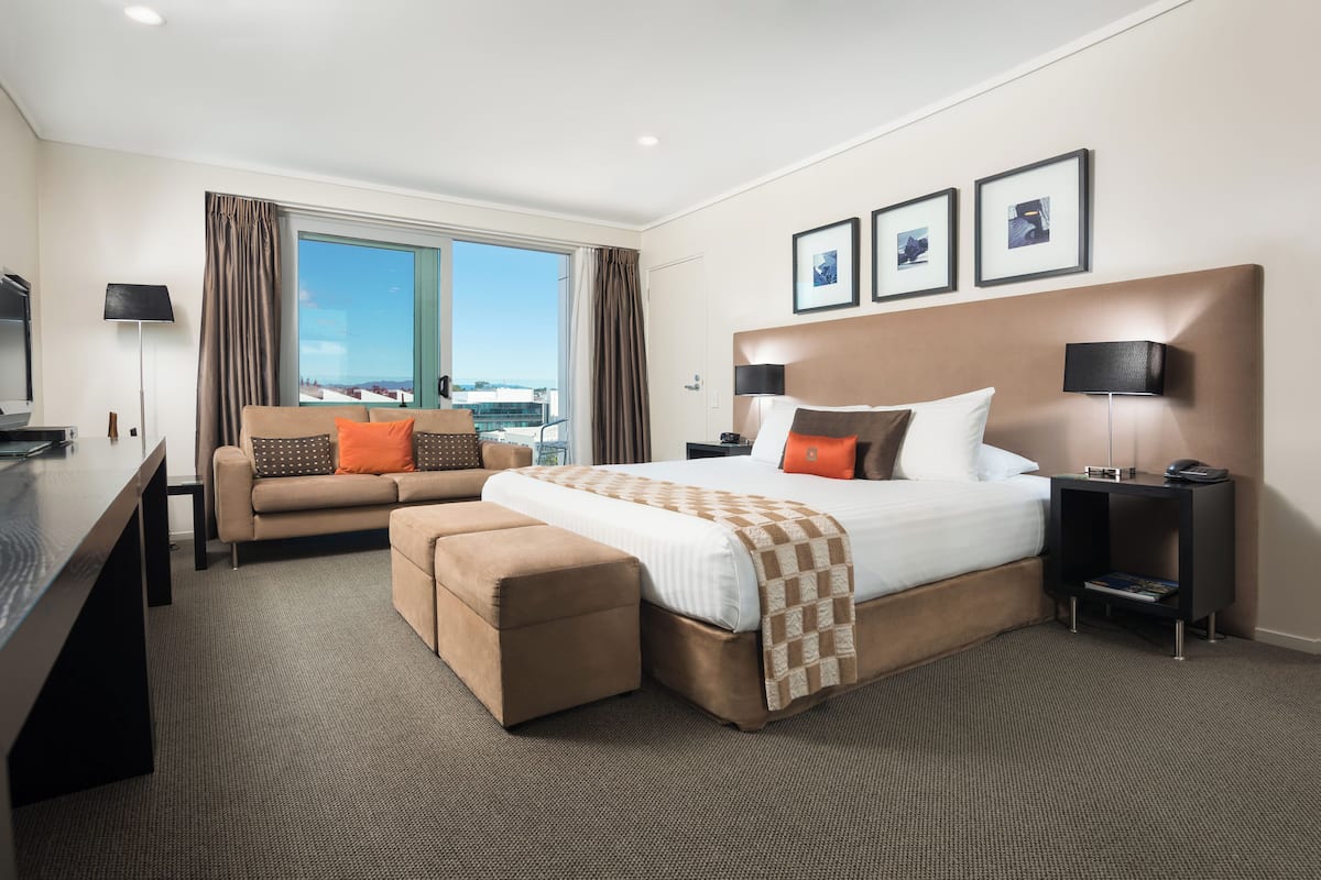 A hotel room with a large bed, a sofa, a desk, and a view of the city.