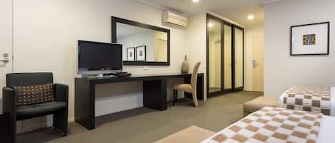 A hotel room with a desk, television, two beds, a chair, and a mirror.