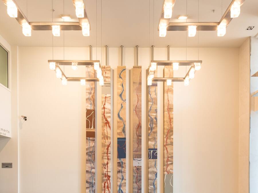 A modern lobby with a central seating area, a decorative wall with abstract patterns, and a series of pendant lights.