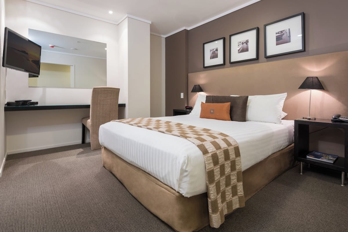 A hotel room with a large bed, a desk, a chair, a TV, and framed pictures on the wall.