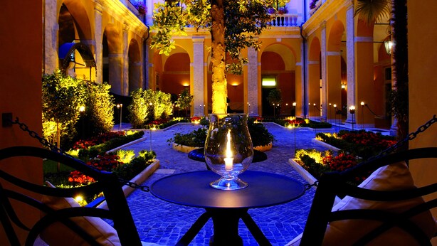 A courtyard with a central table, surrounded by chairs, and a candle in a glass holder. - Palazzo Cardinal Cesi (Rome)