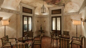 A room with a round table and chairs, a chandelier, and two windows with curtains. - Palazzo Cardinal Cesi (Rome)
