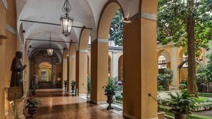 A corridor with arches, potted plants, and a statue. - Palazzo Cardinal Cesi (Rome)