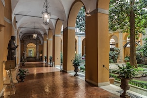 Un pasillo con arcos, plantas en macetas y una estatua.