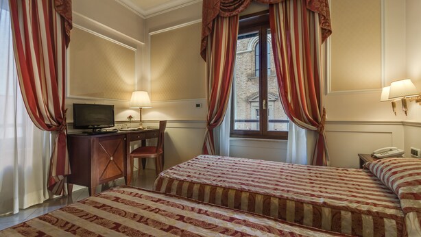 A hotel room with two beds, a desk with a television, and a window with curtains. - Palazzo Cardinal Cesi (Rome)
