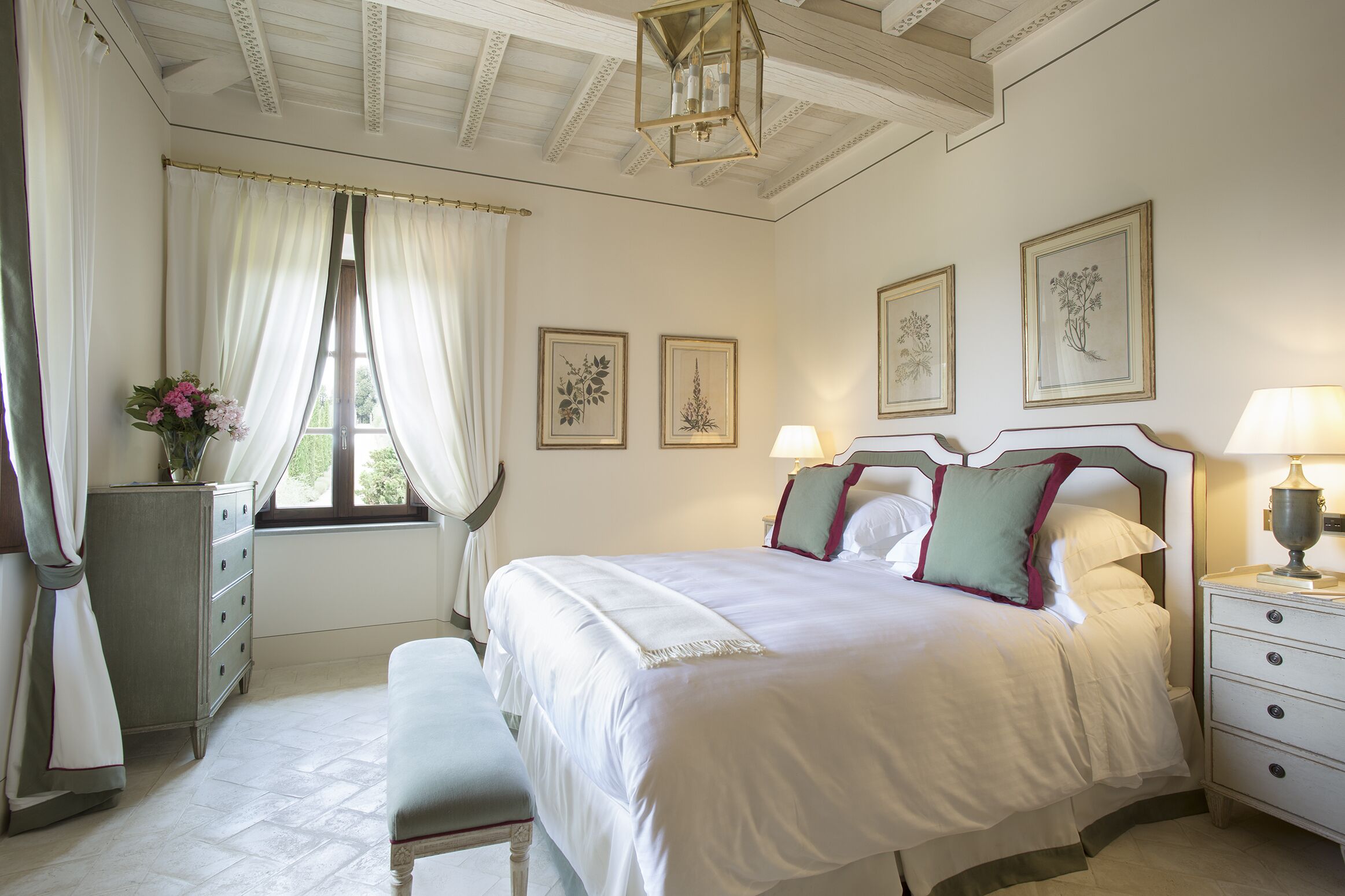 A bedroom with a large bed, a dresser, a bench, and a window with curtains.