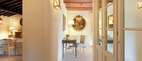 A hallway with a dining area, featuring a table and chairs, a lamp, and a wall-mounted painting.
