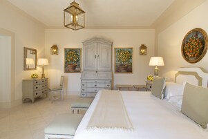 Un dormitorio con una cama grande, un tocador, una silla y dos mesitas de noche con lámparas.