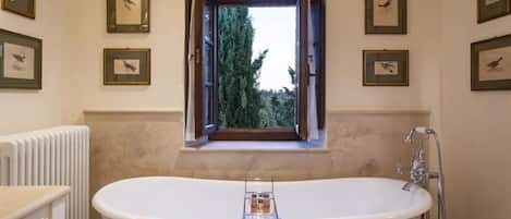 Un baño con una bañera independiente, una ventana con un persiano abierto y fotografías de aves enmarcadas en las paredes.
