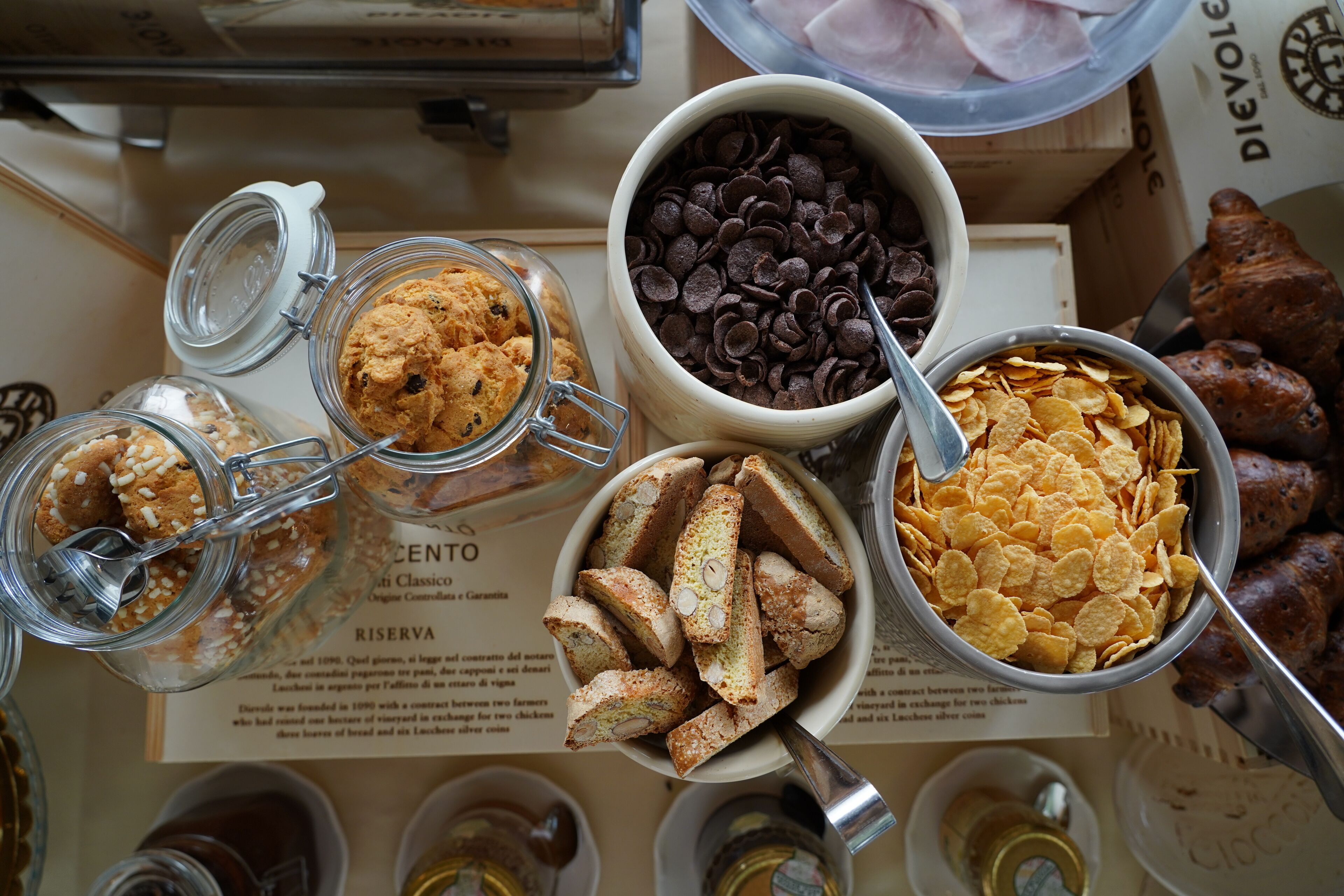 Una mesa con diversos alimentos, como galletas, chips de chocolate, cereales y cruasanes.
