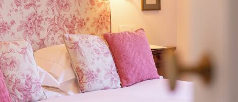A neatly made bed with floral-patterned pillows and a headboard, a bedside lamp, and framed pictures on the wall.