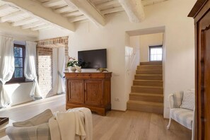 A spacious living room with a wooden staircase, a TV on a wooden cabinet, and a cozy seating area.