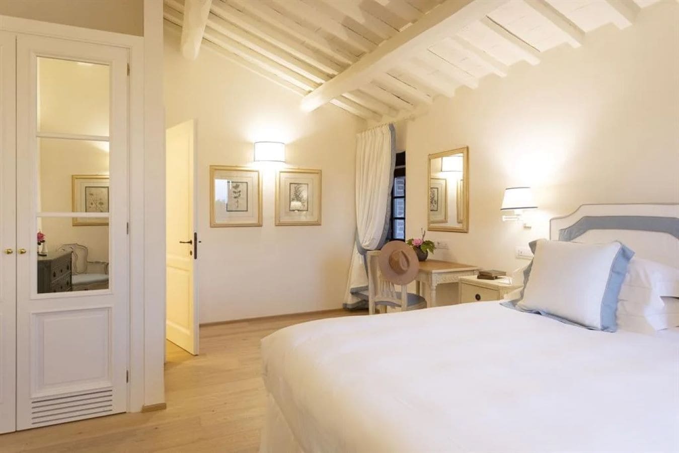 Habitación de hotel con cama, escritorio y silla. Cuadros enmarcados en la pared y un espejo sobre el escritorio.