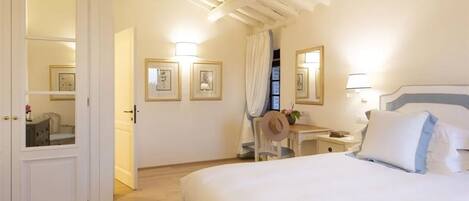 Habitación de hotel con cama, escritorio y silla. Cuadros enmarcados en la pared y un espejo sobre el escritorio.